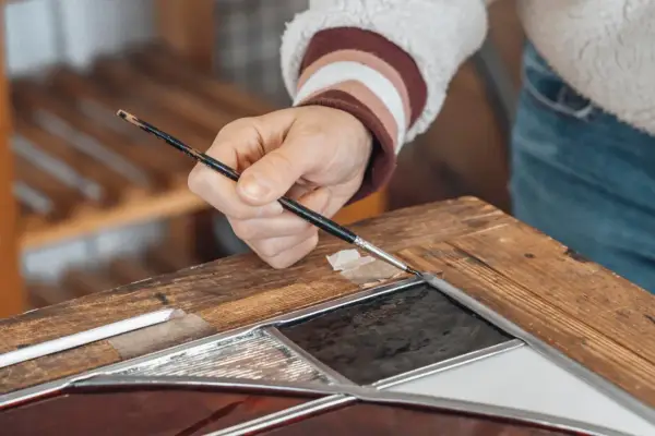 Main d'un artisan travaillant sur un vitrail, un exemple de métiers rares et recherchés.