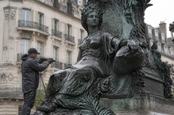 Un homme nettoie une statue en bronze avec un jet d'eau. Il apprend comment nettoyer le bronze pour redonner son éclat à l'œuvre.