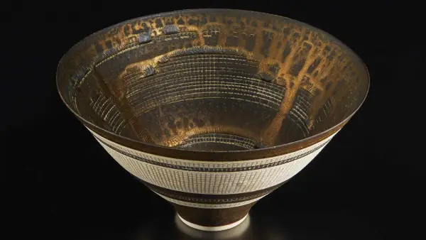 Vase texturé aux reflets dorés et noirs, œuvre d'un céramiste connu, évoquant une cité futuriste.