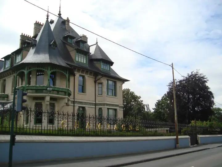 La maison Demoiselle à Reims, une bâtisse de style Belle Époque avec ses toits pointus et sa ferronnerie verte. Le mot "CHAMPAGNE" est visible sur la grille.