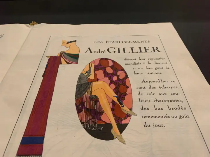 Publicité André Gillier, style art déco, avec une femme aux jambes ornées de bas brodés, rappelant les dates de cette époque.
