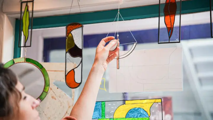 Une main ajuste un vitrail coloré, œuvre d'un fabricant de vitraux, devant une fenêtre.