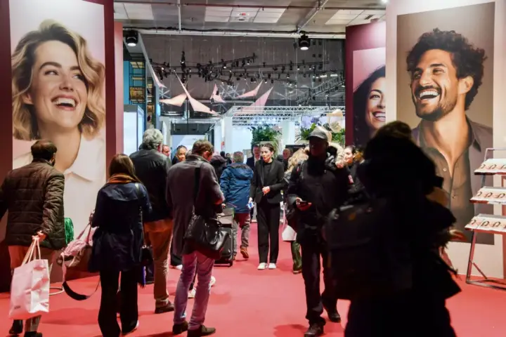 Foule dans un salon, devant de grandes affiches publicitaires. L'esprit meuble est palpable, les gens déambulent, curieux.