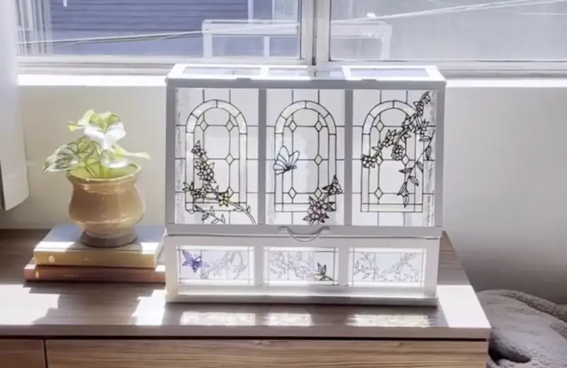 Boîte à bijoux ornée de vitraux décoratifs représentant des papillons et des fleurs, posée sur une commode en bois.