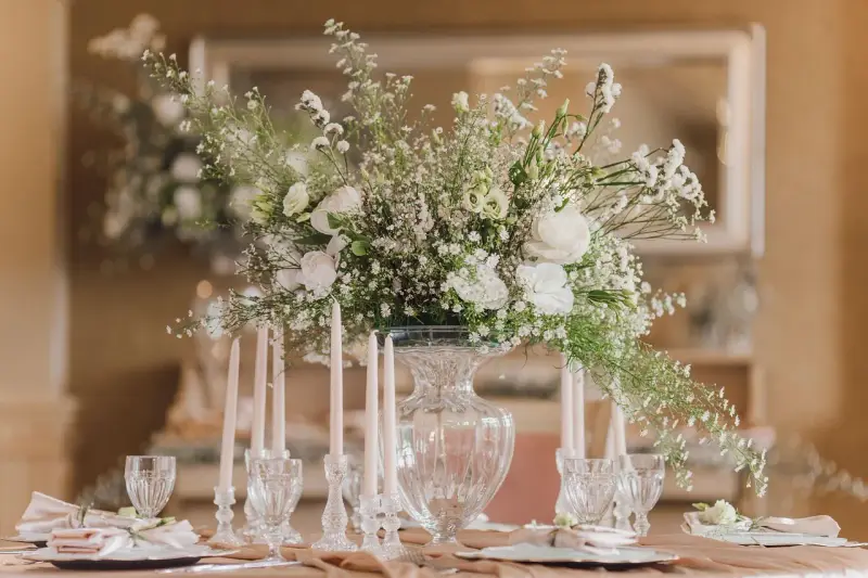 Un bouquet de vitrail fleur, blanc et aérien, orne une table dressée avec des bougies et des verres délicats.